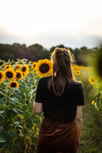 Rear view of woman standing by sunflower plants against sky