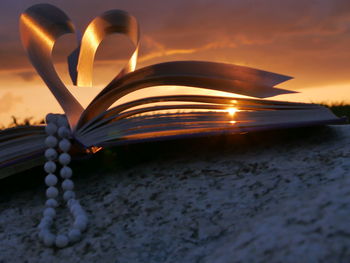 Bead necklace with heart shape folded pages of book during sunset