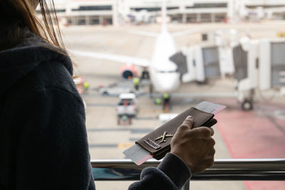 Midsection of woman holding passport and ticket by railing at airport