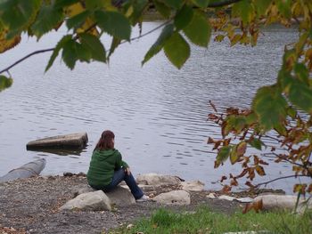 Rear view of woman sitting on rock by lake