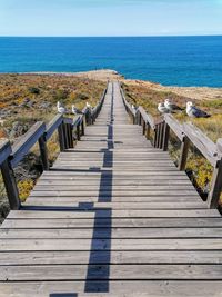 Wooden walkway leading towards sea against sky