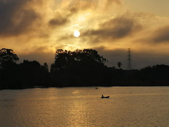 Silhouette person in sea against sky during sunset