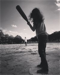 Rear view of girl holding baseball bat standing on beach