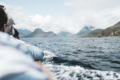 People enjoying on boat amidst scenic sea by mountains against sky