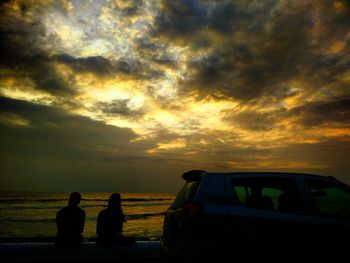 Silhouette people sitting by sea against sky during sunset