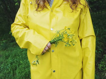 Midsection of woman wearing yellow raincoat while holding flowers