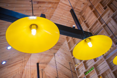 Low angle view of yellow light bulb hanging on ceiling