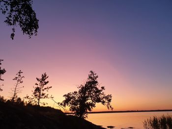 Silhouette trees by lake against romantic sky at sunset