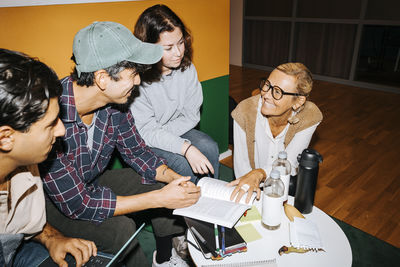 Smiling female teacher crouching while assisting male student in studies at tech college