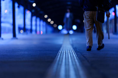 Low section of person walking on illuminated street at night