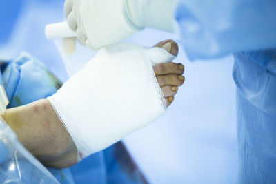 Cropped image of surgeon wrapping bandage on patient wounded foot