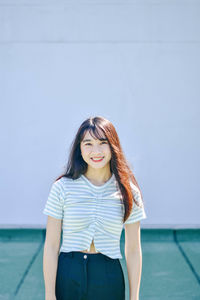 Portrait of young woman smiling while standing against wall