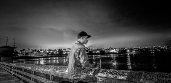 Blurred motion of man by railing against river in city at night
