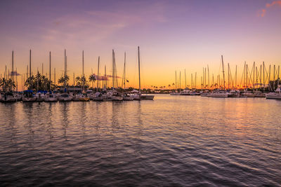 Sailboats moored on sea against sky during sunset