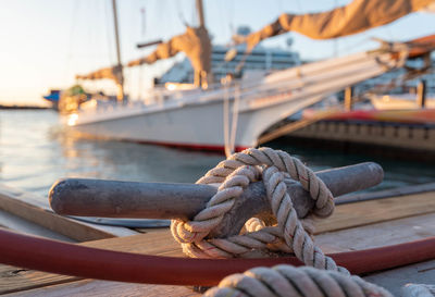 Close-up of rope tied on pier with yacht in background