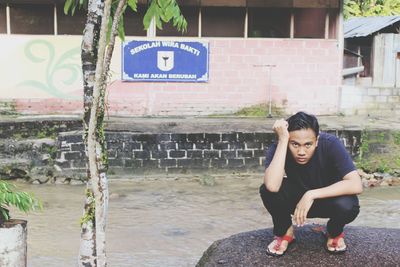 Portrait of man crouching on rock against building