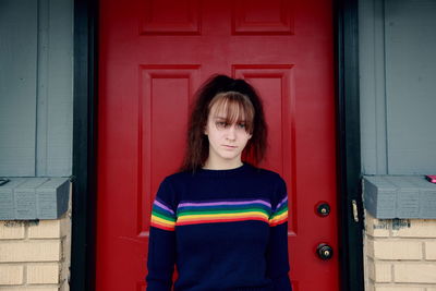 Portrait of young woman standing against red door