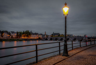 Illuminated street light by river against sky at night