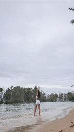 Rear view of woman standing at beach against sky