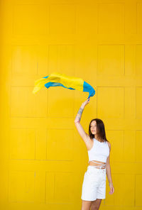 Rear view of woman holding umbrella against yellow background