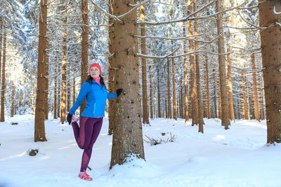 Mid adult woman standing on snow covered field by tree in forest