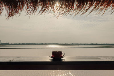 Coffee cup on table by lake against sky