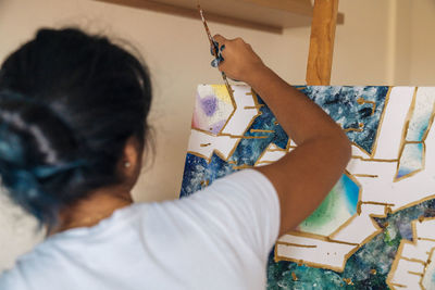 Back view anonymous female painter in white shirt drawing lines on easel in light studio