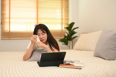 Young woman using laptop while sitting on bed at home