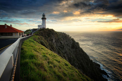 Lighthouse amidst sea and buildings against sky during sunset