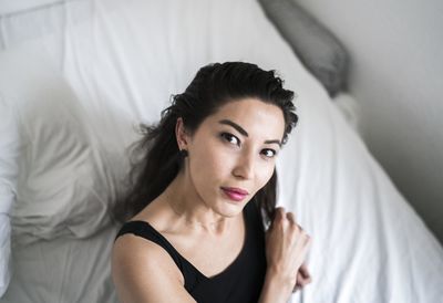 High angle portrait of young woman sitting on bed at home