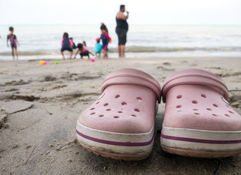 People enjoying on shore at beach with shoes in foreground