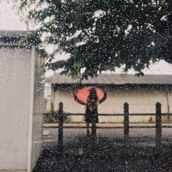 Girl with umbrella seen through wet window during rainy season