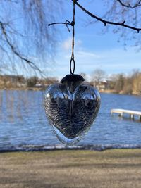 Close-up of decoration hanging on tree by lake against sky