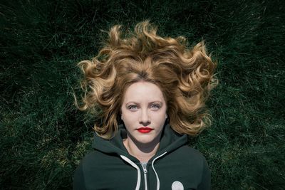 Portrait of young woman with blond hair lying down on grassy field