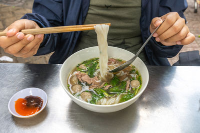 Human hand using chopsticks while having pho noodle soup