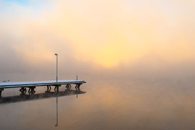 Snow covered pier over calm lake during foggy weather