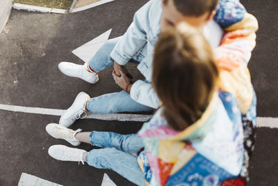 Top view of unrecognizable young couple sitting between the signs on the floor of a skate park