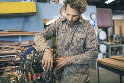 Carpenter arranging tools in belt at workshop