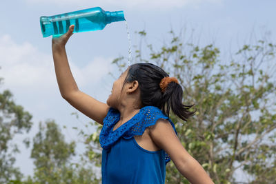 Side view of young woman drinking water at park