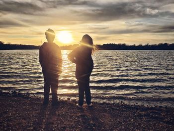 Silhouette friends standing on beach against sky during sunset