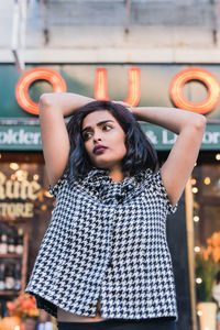 Young woman standing with hand in hair against shop