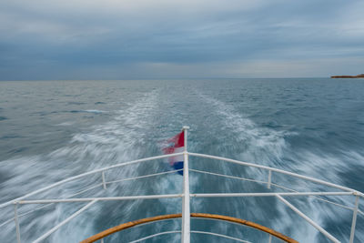 Cropped image of boat sailing on sea against cloudy sky