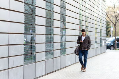 Young bearded man walking in the street while using a smartphone