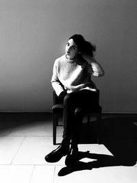 Portrait of young woman sitting on chair against wall