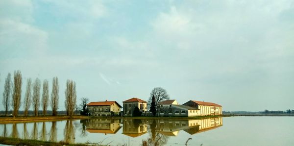 Houses by lake and buildings against sky