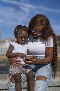 Woman sharing mobile phone with daughter on sunny day