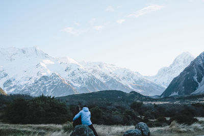 Rear view of couple looking at snowcapped mountains against sky