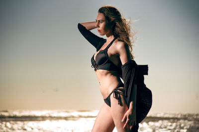 Woman in bikini standing at beach against sky