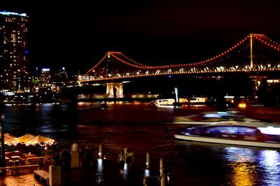 Illuminated suspension bridge over river in city at night