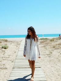 Young woman walking on beach against clear sky